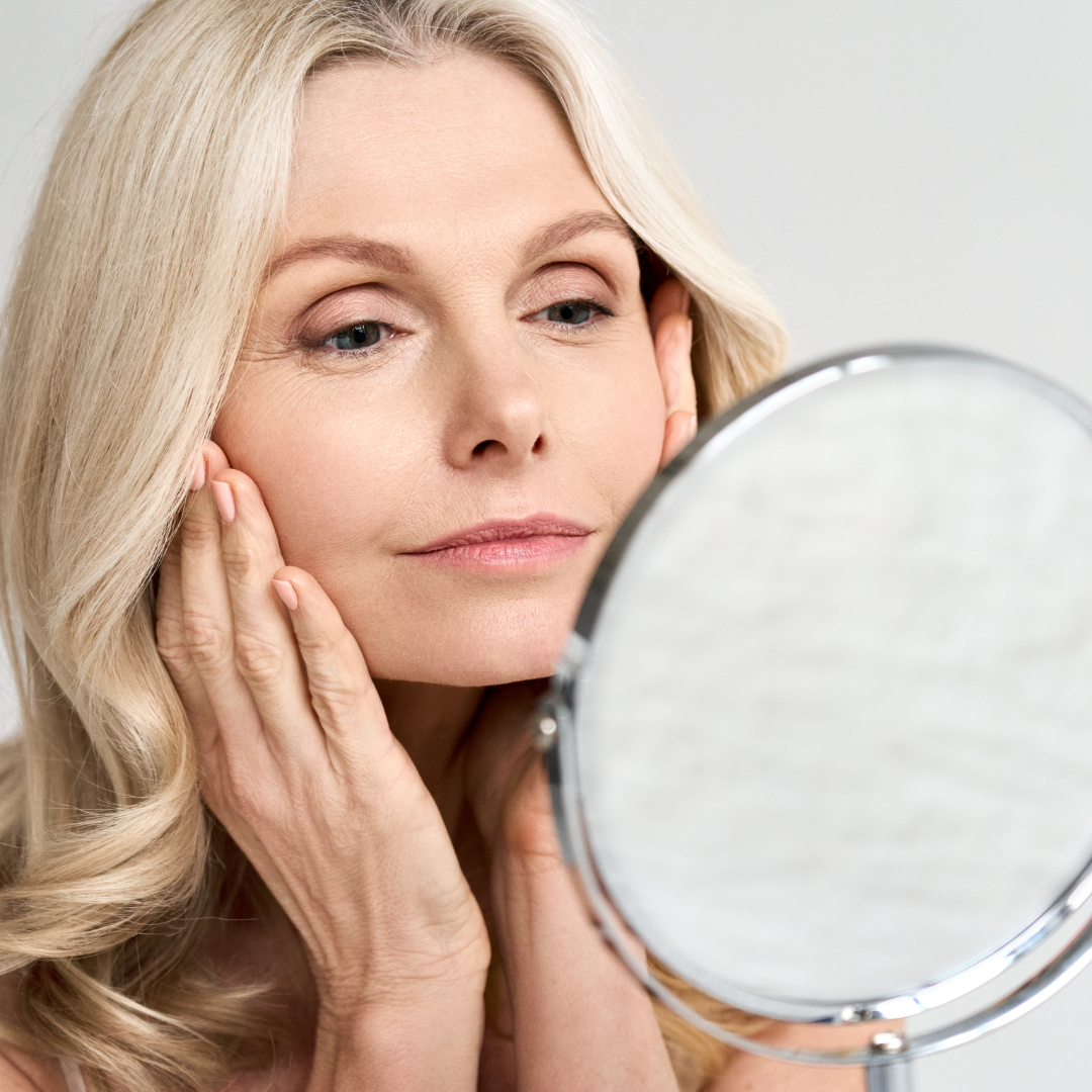 Woman looking closely in mirror at her skin changes due to menopause
